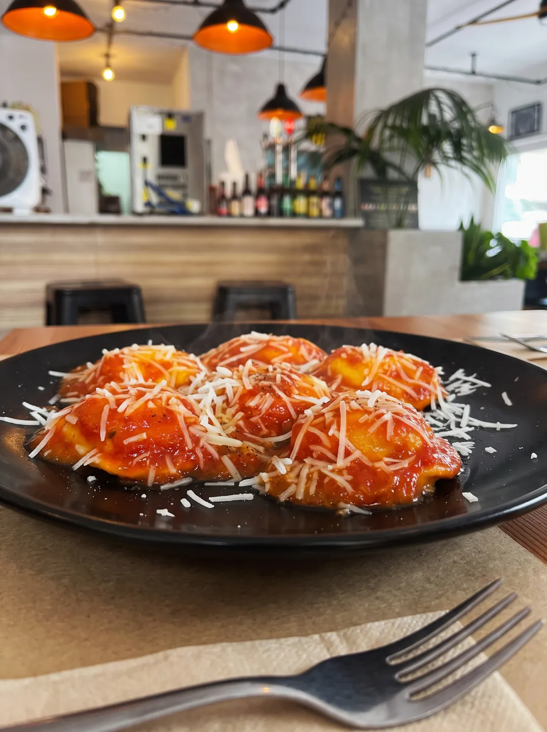 Plato negro con pasta rellena, salsa de tomate y queso rallado