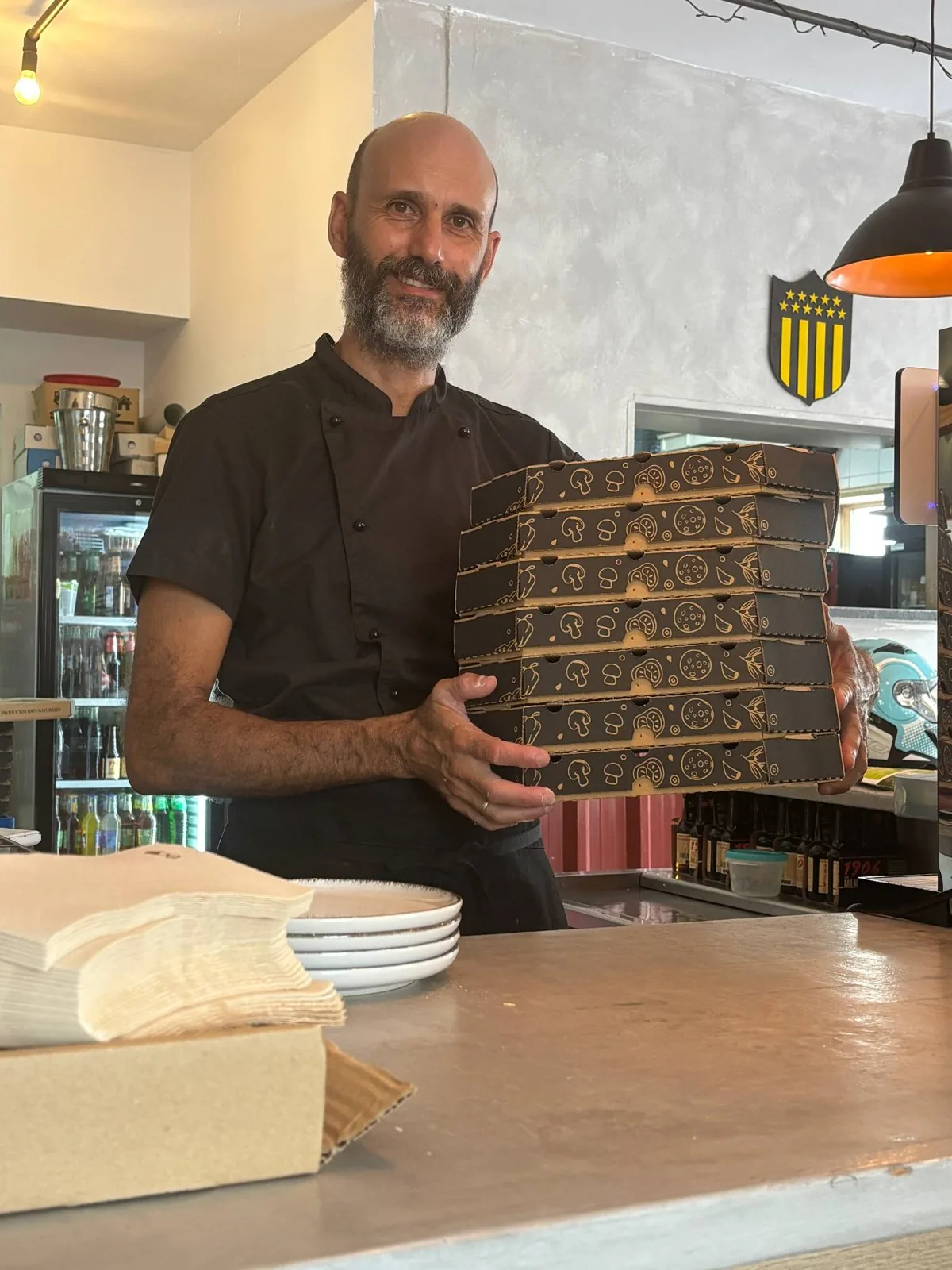 Gonzalo, el dueño de Cabano, sonríe con una pila de cajas de pizza sobre el mostrador